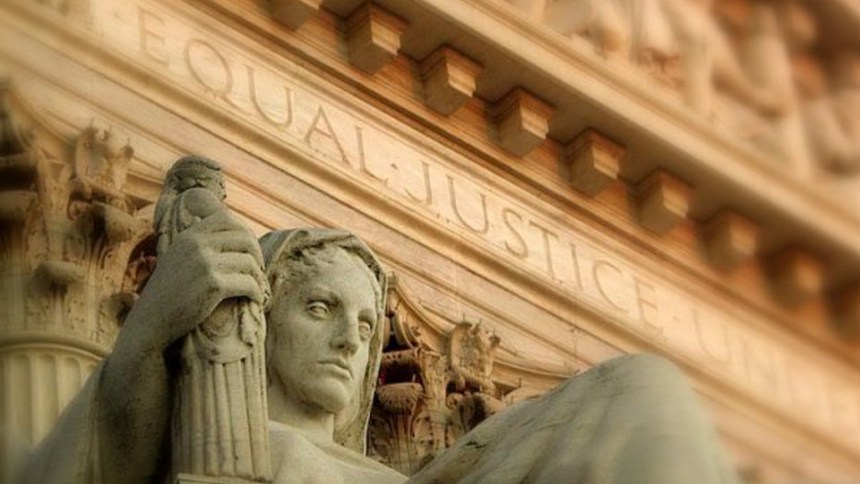 Statue of Lady Justice holding scales, set against a backdrop inscribed with "EQUAL JUSTICE UNDER LAW."