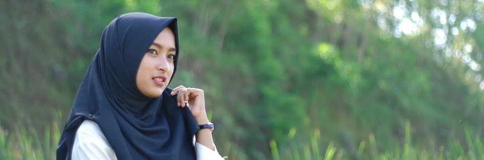 Young woman wearing a hijab, thoughtfully posing outdoors in a green natural setting.