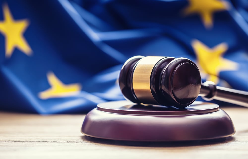 Gavel on wooden surface with European Union flag in the background, symbolizing legal proceedings.