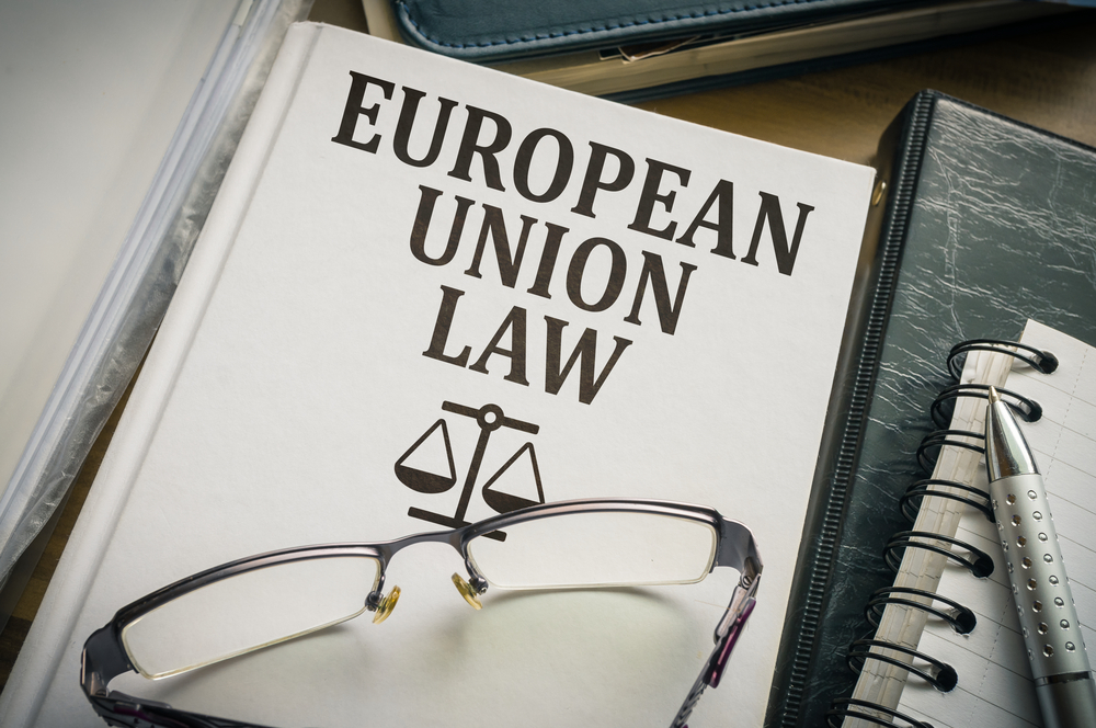 European Union law book with scales of justice, glasses, and legal notepad on a work desk.