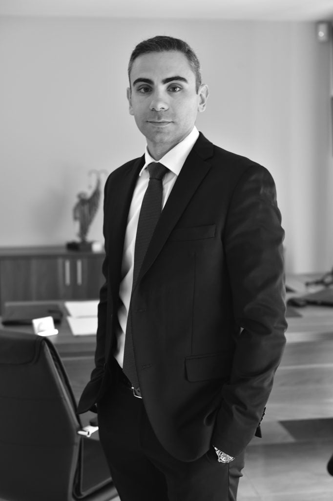 Attorney standing confidently in a law office, dressed in a suit with a modern desk in the background.
