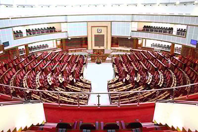Legislative assembly chamber with red seating in a structured arrangement around a central podium.