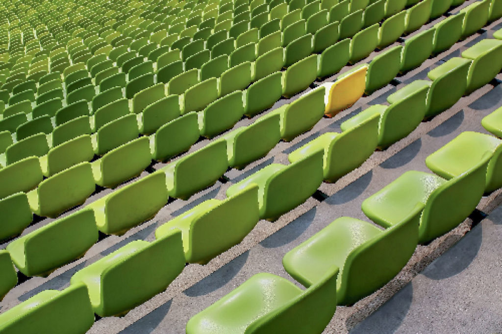 Empty rows of green stadium seats with one yellow seat standing out among them.