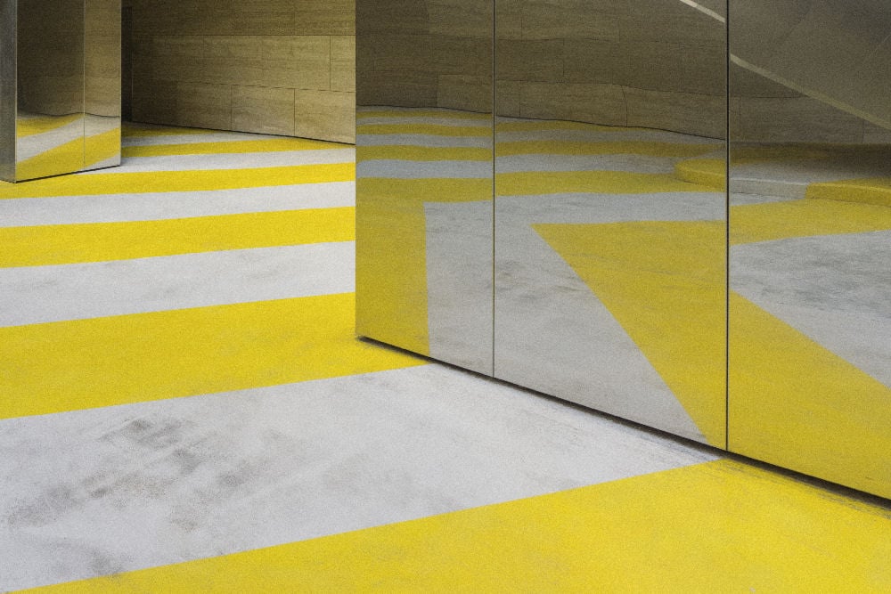 Mirrored walls reflecting a yellow-striped floor in a modern architectural space.