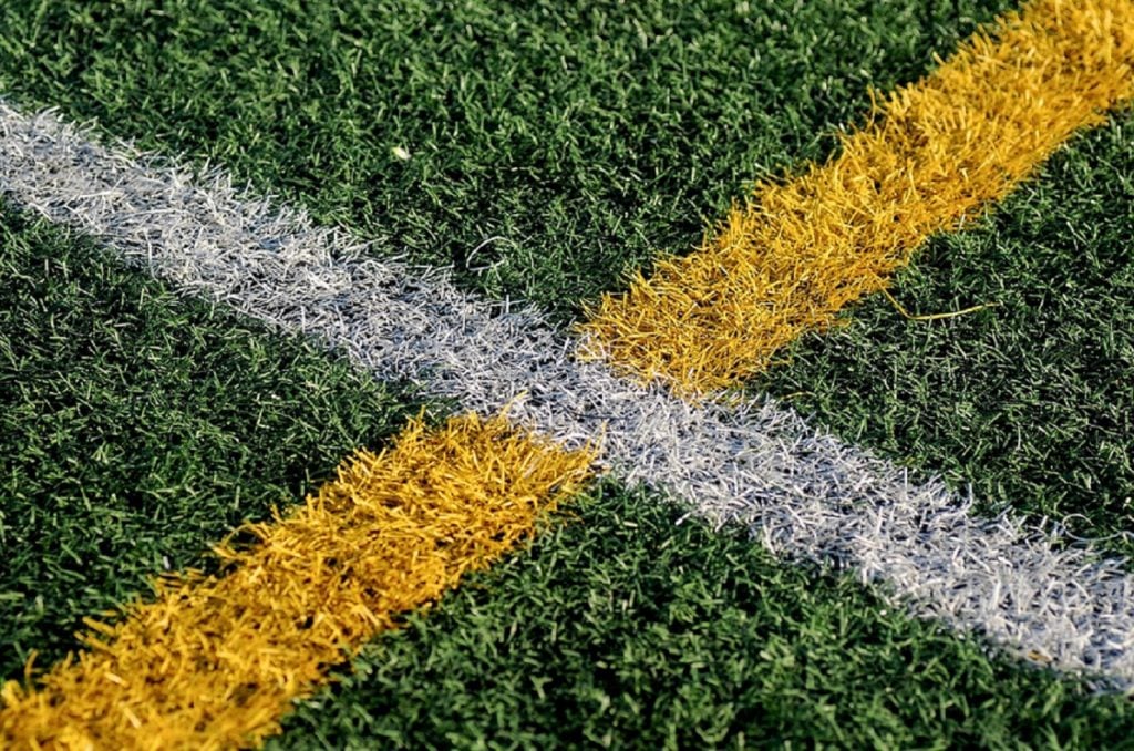 Green artificial turf with white and yellow lines marking a sports field boundary.