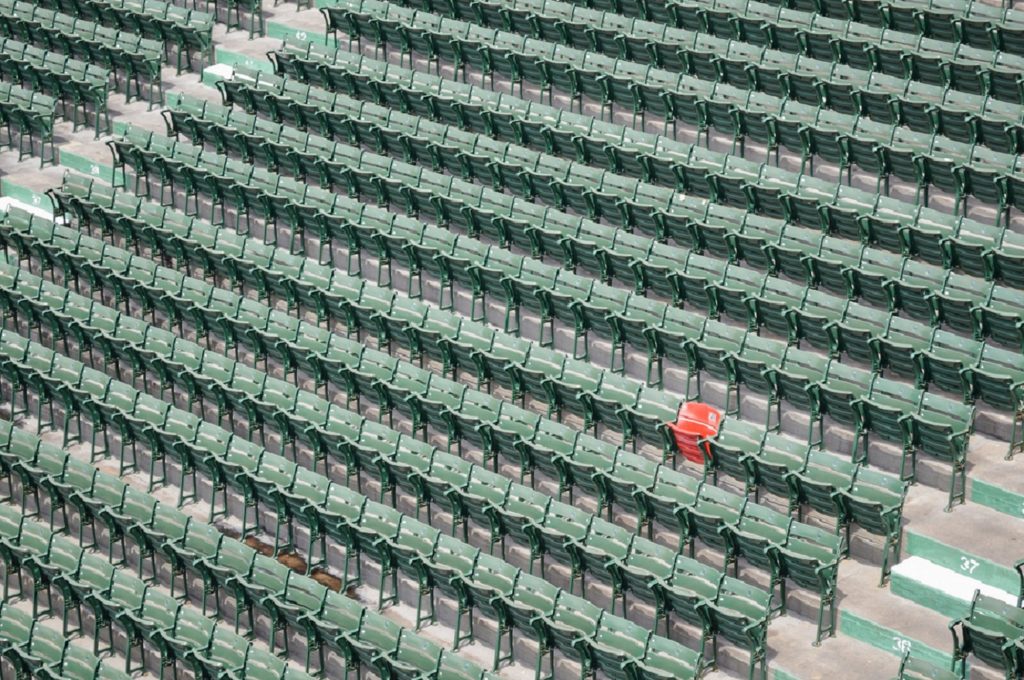 Empty stadium seating with a single red chair amidst rows of green chairs.