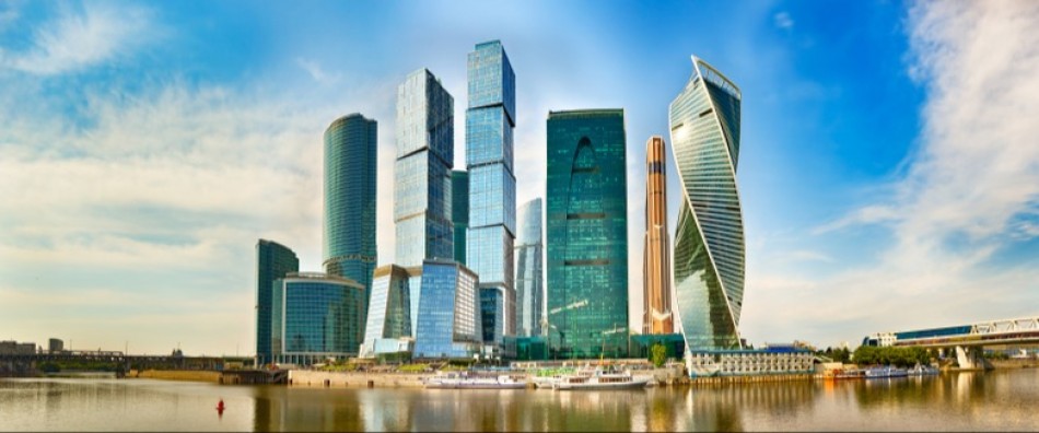 Modern skyscrapers along waterfront with clear blue sky and reflected clouds.