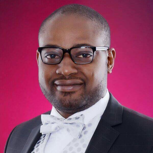 Professional man in a suit with glasses and a bow tie, portrait against a pink background.