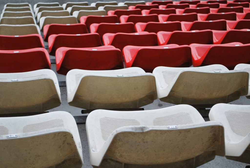 Rows of empty plastic stadium seats in red and beige arranged in a patterned layout.