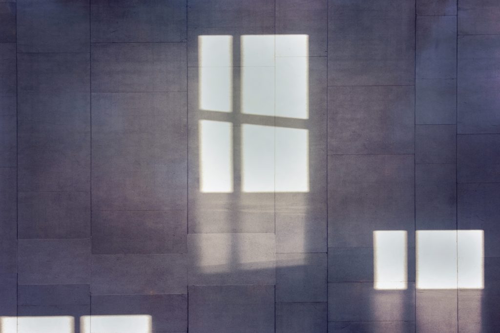 Light patterns created by windows reflected on a textured wall.
