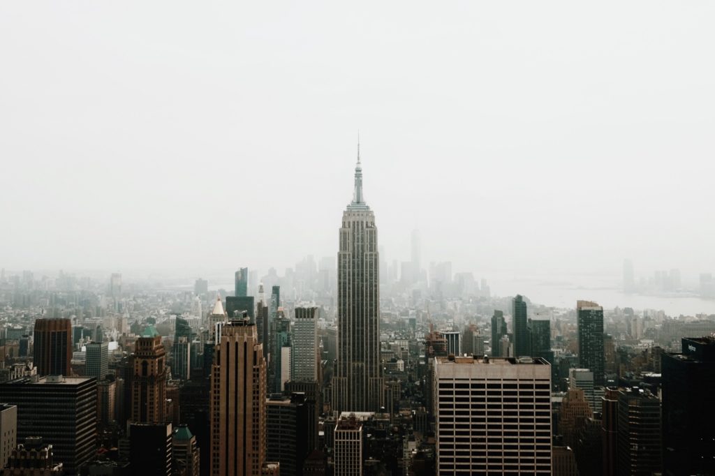 City skyline featuring the Empire State Building among tall skyscrapers under a hazy sky.