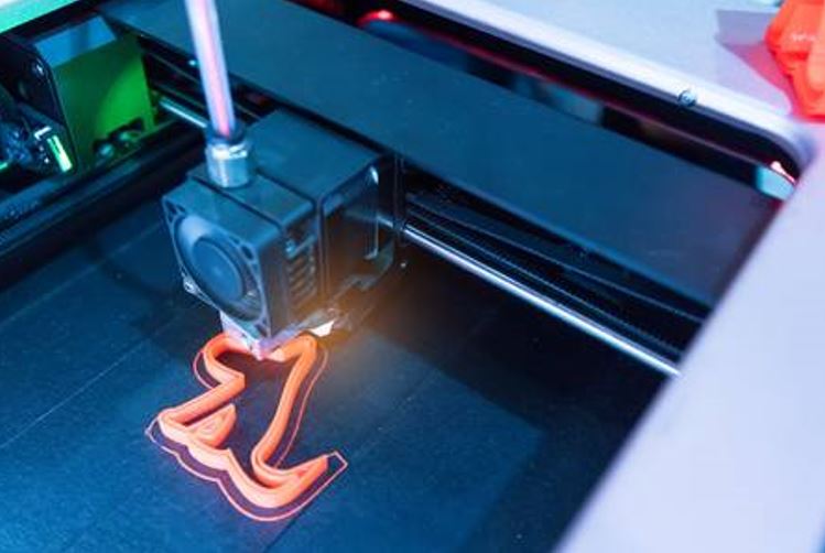3D printer creating a red plastic object on a build plate in a modern workspace.