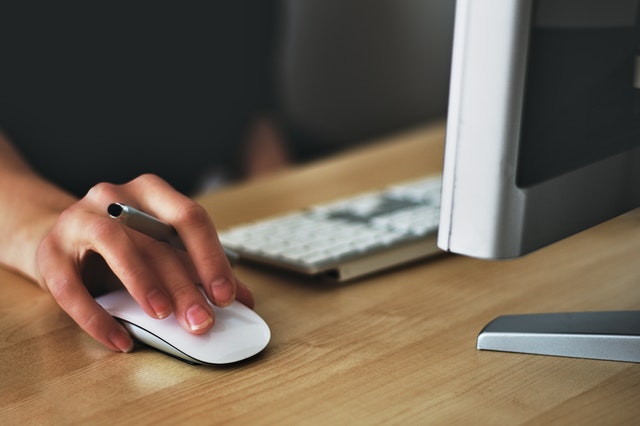 Person using a computer mouse while seated at a desk with a keyboard in an office setting.