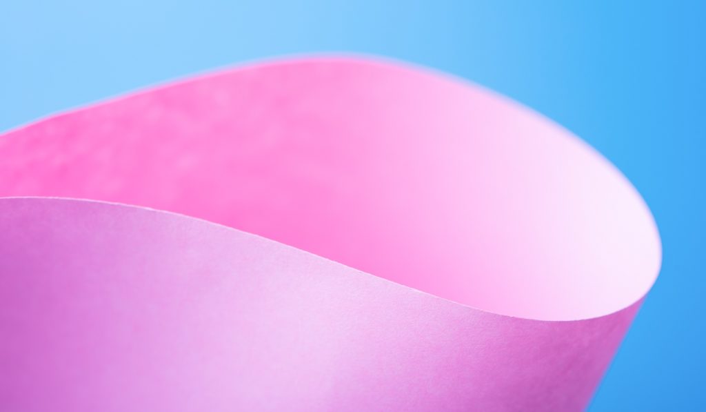 Curved pink paper against a blue background, creating a smooth, abstract visual effect.