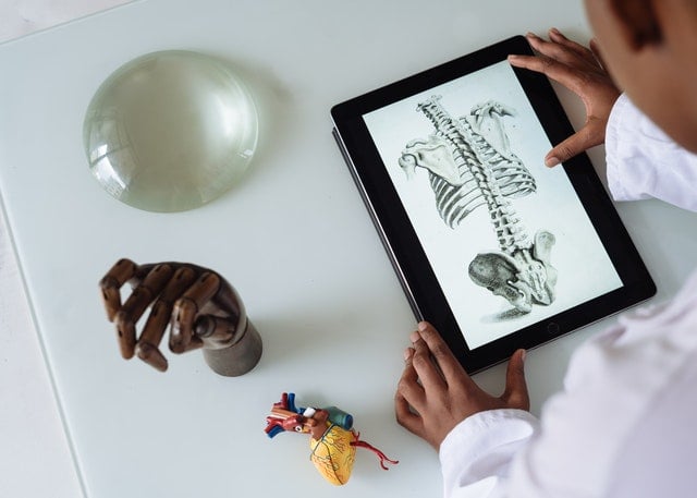 Child holding a tablet displaying a skeletal anatomy illustration, with educational models on table.