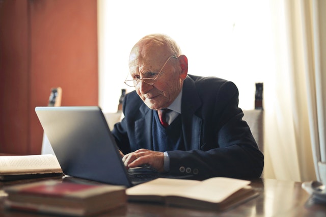 Elderly man working on a laptop at a desk with legal books in a well-lit office setting.
