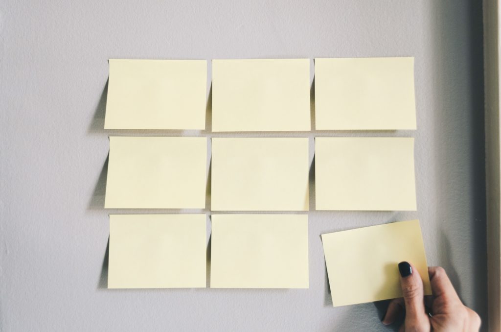 Hand placing a yellow sticky note on a wall with several other notes in a grid layout.