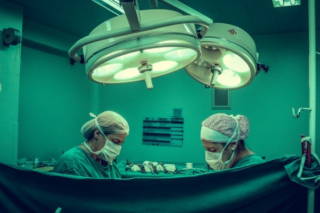 Surgeons performing a medical procedure in an operating room with surgical lights overhead.