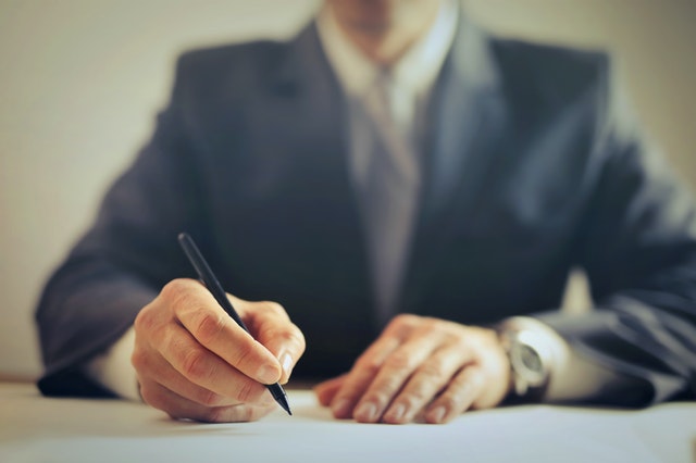 Lawyer signing documents with a pen at a desk in a professional setting.