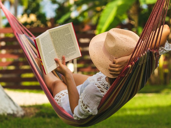 Woman relaxing in a hammock, reading a book in a tropical garden setting.