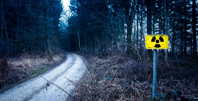 Winding dirt road in forest with a yellow radiation warning sign beside the path.