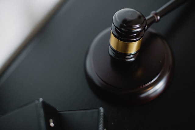 Gavel resting on a desk beside a legal document wallet in a courtroom setting.