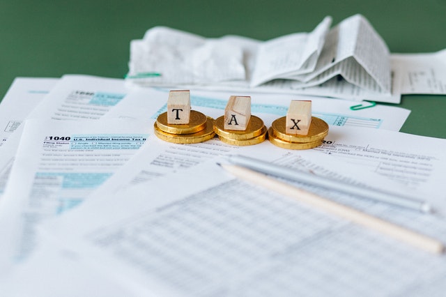 Tax documents and coins labeled "TAX" arranged on a table with receipts and a pencil.