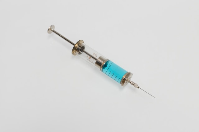 Syringe filled with blue liquid, positioned on a neutral background.