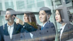 Group of professionals in suits discussing ideas in a modern office setting with large windows.