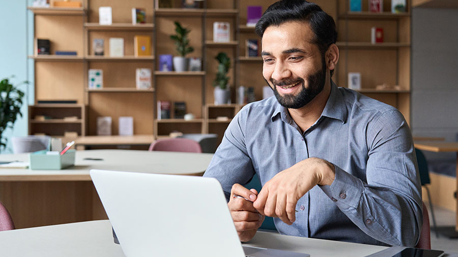 Professional consulting on a laptop in a modern office setting with bookshelves in the background.