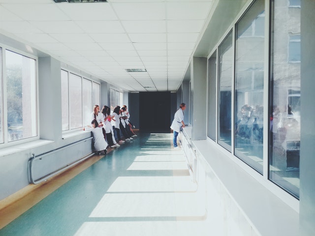 Group of medical professionals in white coats observing from hospital hallway with large windows.
