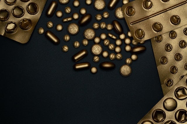 Gold and black assortment of pills and capsules scattered across a dark surface.
