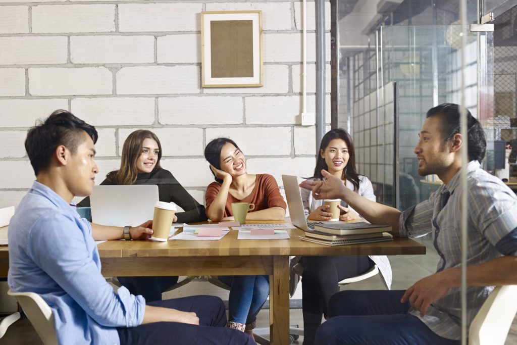 Group of professionals discussing ideas around a conference table with laptops and coffee cups in a modern office.