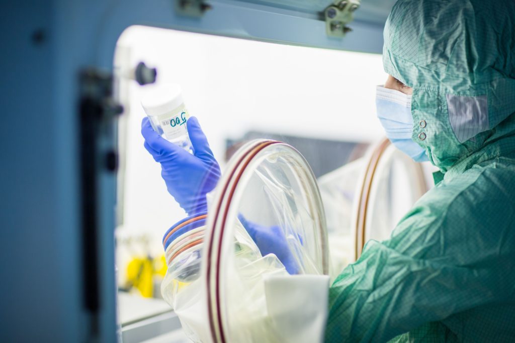 Laboratory technician in protective gear examining a vial inside a clean room environment.