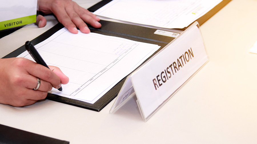 Visitor completing a registration form at a reception desk with a sign labeled "Registration" nearby.