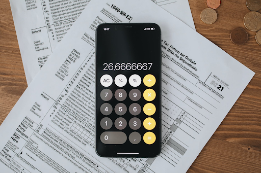 Calculator displaying numbers on top of tax documents and coins on a wooden surface.