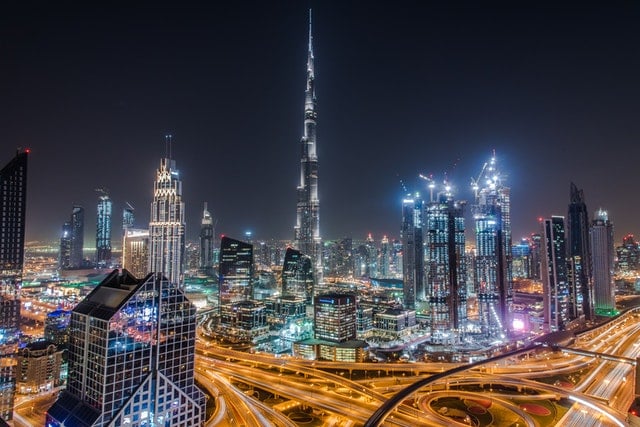 City skyline at night featuring Burj Khalifa and illuminated skyscrapers with busy roadways below.