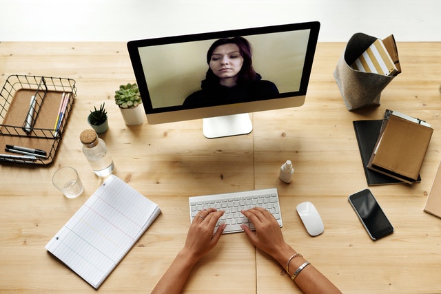 Individual engaged in video conference at a wooden desk with a computer, stationery, and plants.