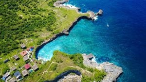 Aerial view of a coastal landscape with rocky shores and vibrant blue water surrounding green hills.