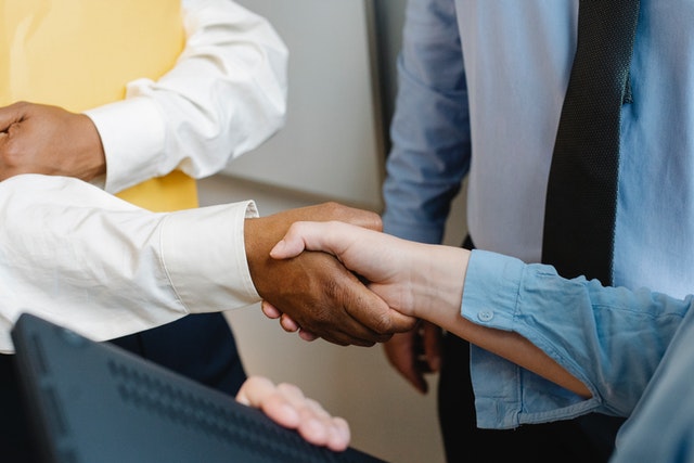 Three professionals shaking hands in a business setting, indicating a legal agreement or collaboration.