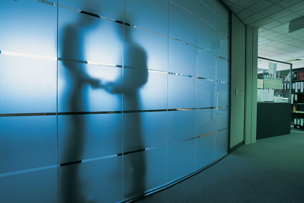 Two silhouettes shaking hands through frosted glass in a law office, indicating a negotiation or agreement.