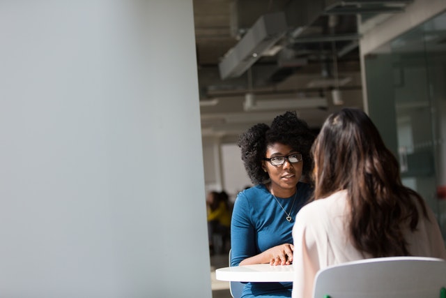 Two women engaged in a consultation at a table in a modern office setting.
