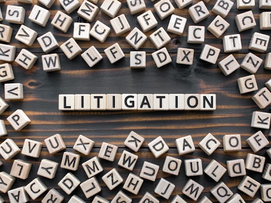 Wooden letter tiles arranged on a table, spelling "LITIGATION" amidst various other letters.