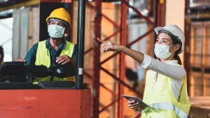 Female construction manager directing work at a construction site, while a forklift operator observes.