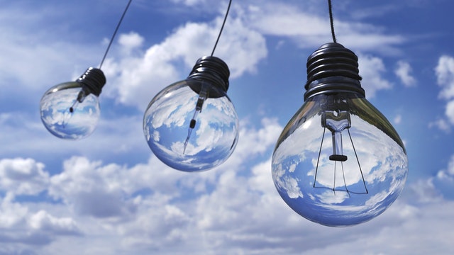 Hanging light bulbs reflecting clouds and blue sky in a bright, outdoor setting.