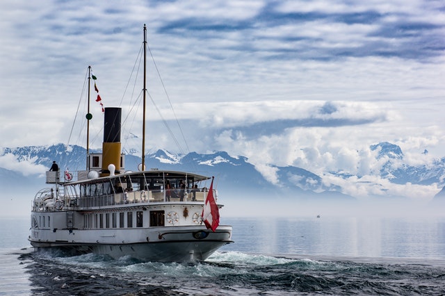 Steamboat navigating calm waters with snow-capped mountains in the background.