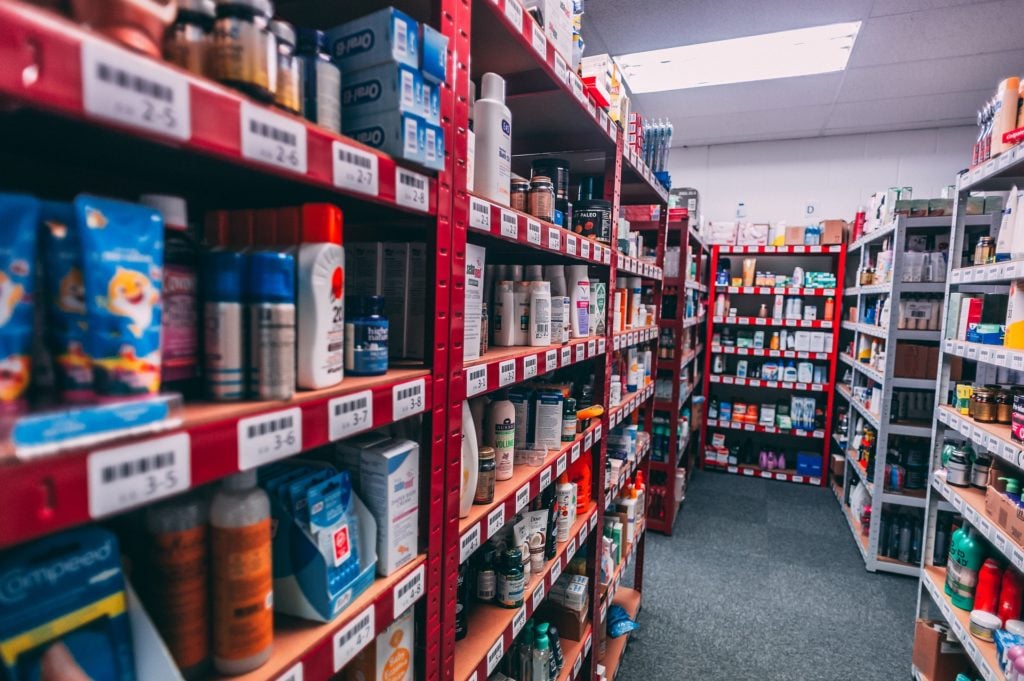 Aisle in a store displaying numerous health and beauty products on red shelves with visible price tags.