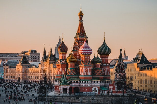 Historic St. Basil's Cathedral with colorful domes, surrounded by people at sunset in a public square.