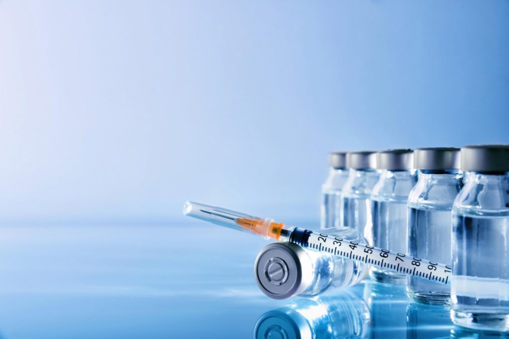 Syringe placed on a table beside multiple vaccine vials in a clinical setting.