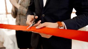 Male lawyer cutting a red ribbon at a formal event, symbolizing an opening or celebration.